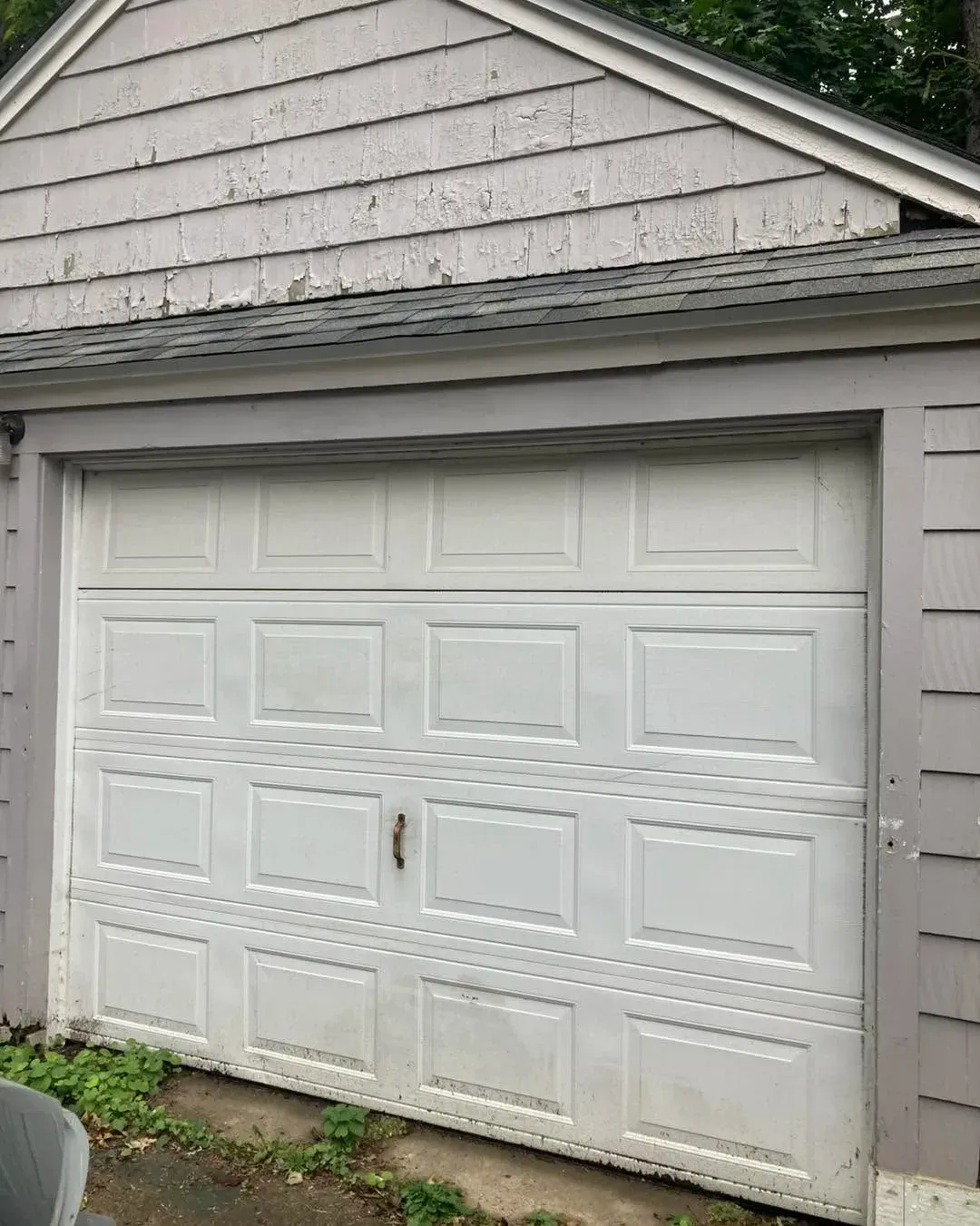 White double garage door on a gray house exterior with weathered siding and a small upper roofline.