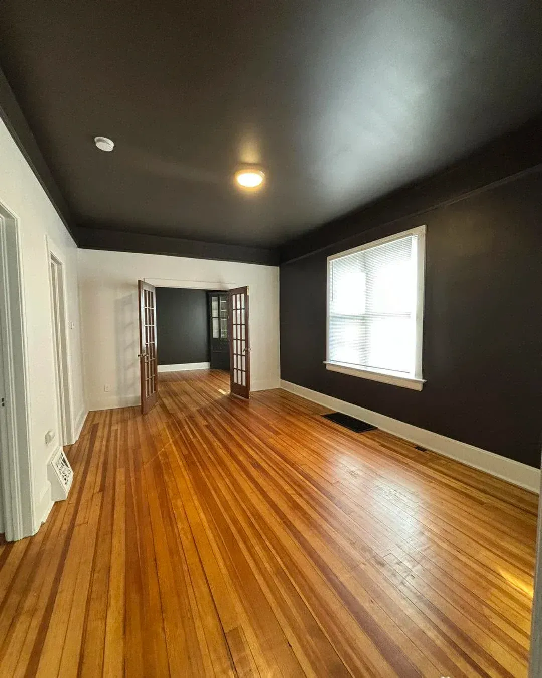 Empty room with dark walls, polished wood floors, and a window letting in daylight. Empty room with dark walls, polished wood floors, and a window letting in daylight.
