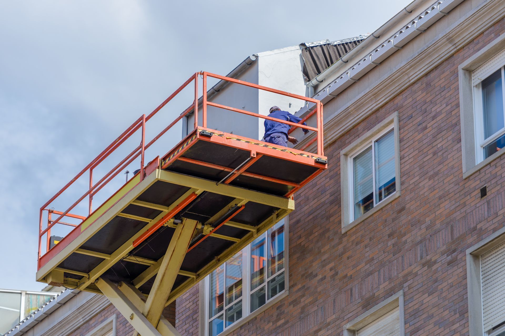 Worker on a scissor lift painting the exterior wall of a brick building.